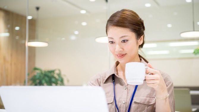 マグカップを片手に席で仕事する女性