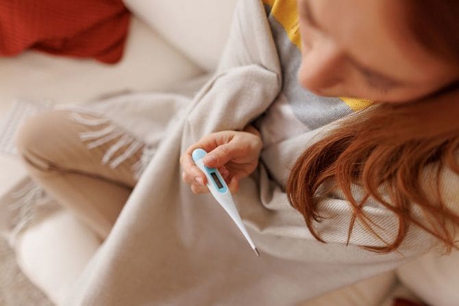 毛布にくるまり、体温計を確認している女性