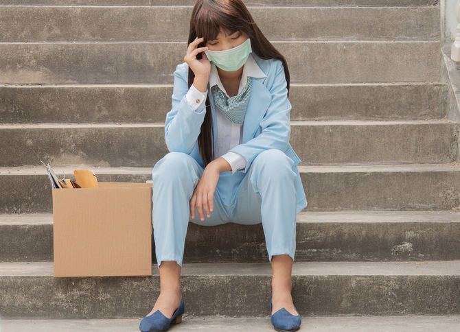 解雇に遭い段ボールにまとめた荷物を横に階段に座り込む女性