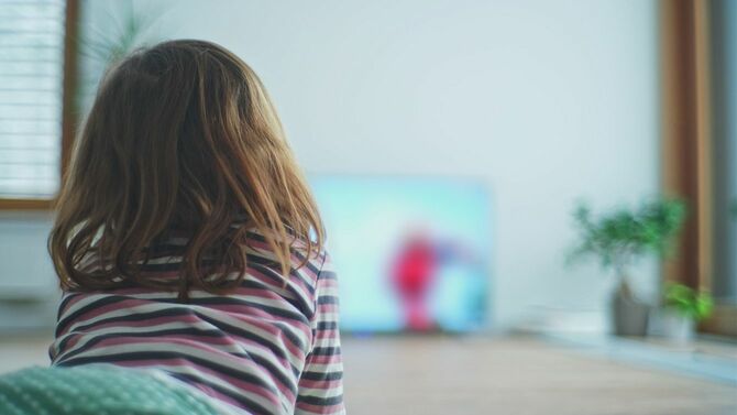 若い白人の女の子は、テレビでアニメーション映画の漫画を見て時間を無駄に床に一人で横たわっている
