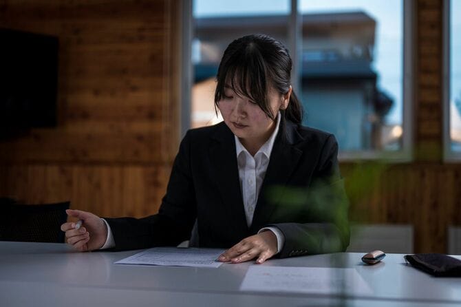 暗い顔で書類を書くスーツの女性