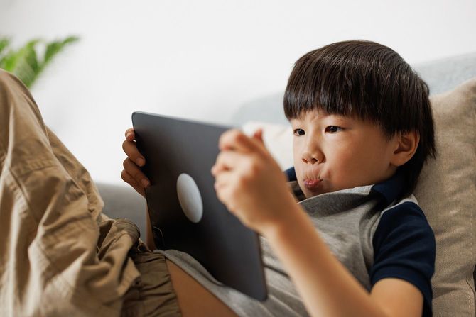 ソファに横たわりタブレットで読書をする男の子