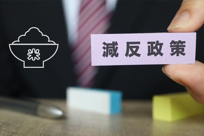 「減反政策」のカードを持つ男性の手元