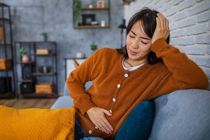 ソファで休んでいるときに腹痛に苦しむ女性
