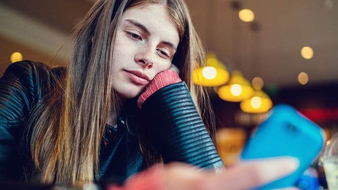 10代の少女がカフェで退屈そうにスマホで文字を打っている