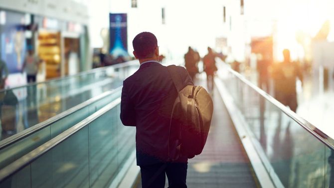 夕暮れ時の空港、歩く歩道をゆくビジネスマンの後ろ姿