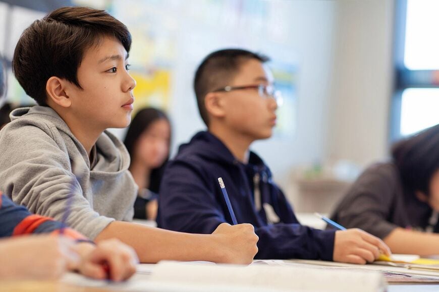 男の子がクラスメートと一緒に小学校の教室で勉強