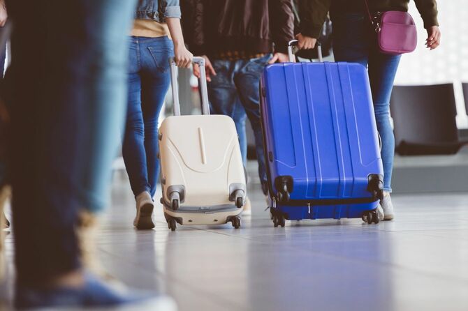 スーツケースを引いて空港ターミナルを移動する人々