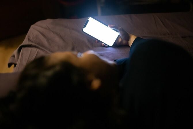 ベッドで寝る前にスマホを見ている女性
