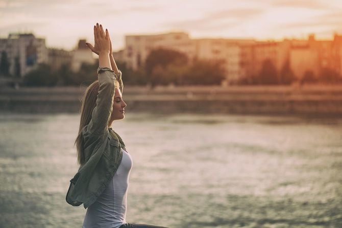 若い女性は川岸で瞑想を楽しんでいます