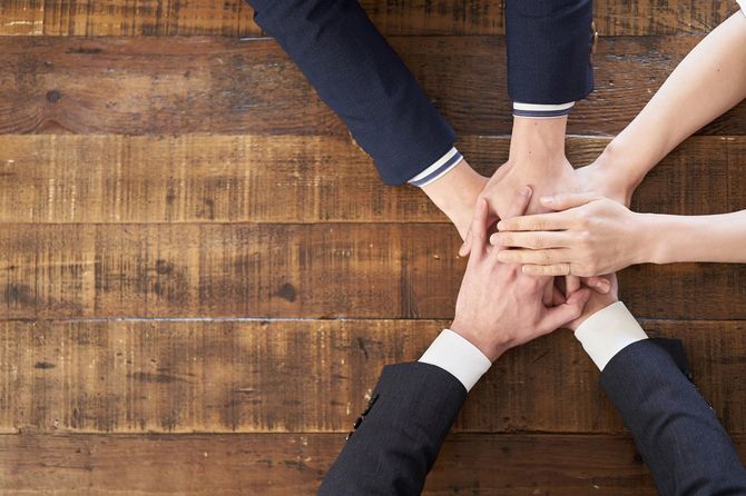 テーブルの上で手を重ねるビジネスパーソン