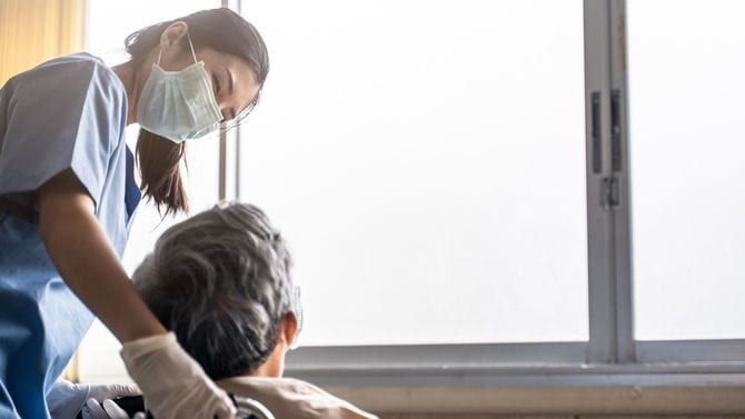 車椅子に座る男性患者の世話をするマスクを着用した女性看護師