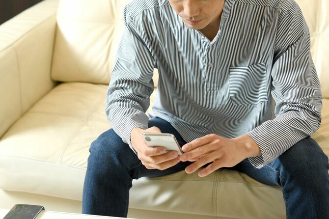 携帯電話を持ちながらソファに座っている若いアジア人男性