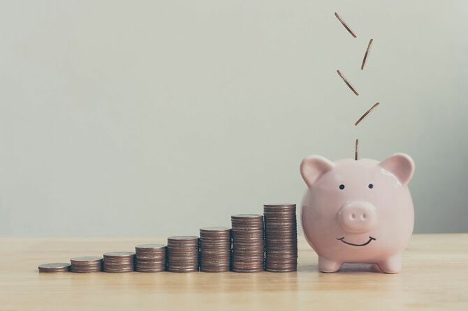 コインが階段状に積み重なった横にあるブタの貯金箱にコインが投入されている