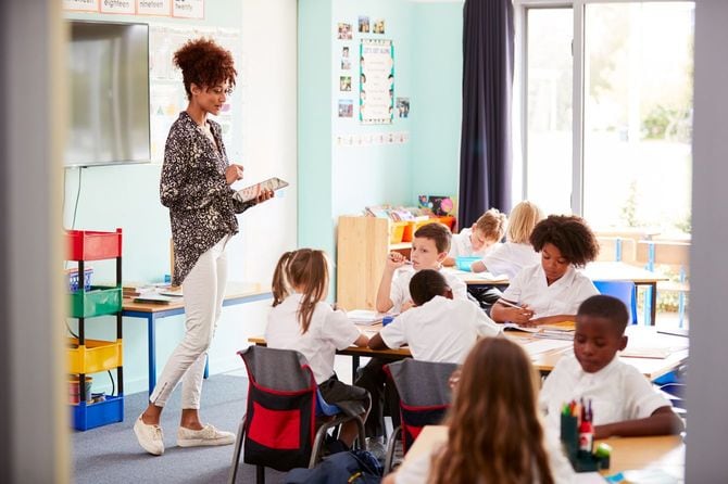 タブレット端末を手に、小学生のクラスで生徒たちを見守る教師