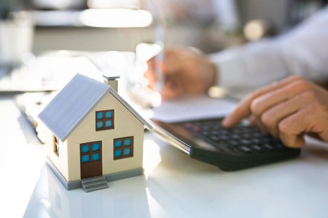 家の模型と電卓を使用する人の手元