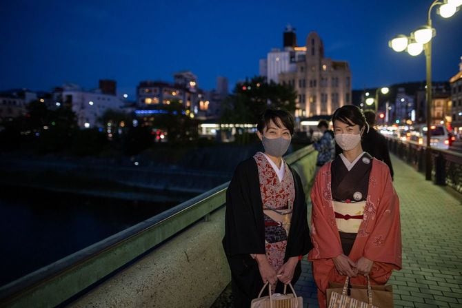 夜の京都でマスクをつけ橋の上に立つ着物を着た日本の女性二人