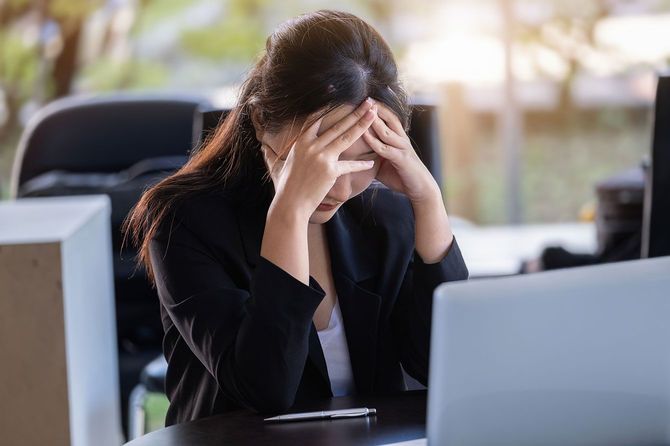 仕事中、デスクで頭を抱える女性