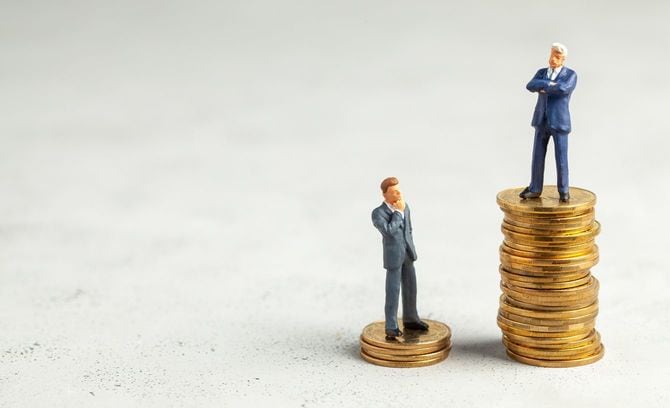 高く積み上げたコインの上にいる成功したビジネスマンと、数枚のコインの上に立つビジネスマン