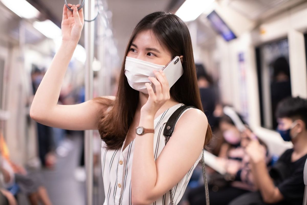 マスクをして電車で電話する若い女性