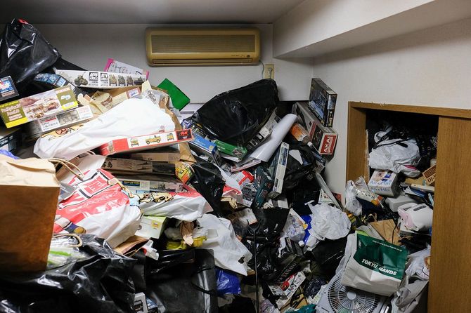 リビングの様子。やはりエアコンの高さまでゴミが積み上がっていた。撮影までに片づけが進んでおり、当初は隣の部屋には入れなかった。エアコンのリモコンはのちほどゴミの中から見つかった。