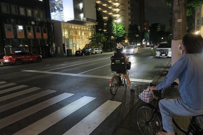 スマホを片手に持つウーバー配達員。しかも大きな道路を逆走しようとしている
