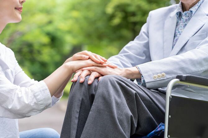 公園で車椅子の老人男性の手を握る若い女性