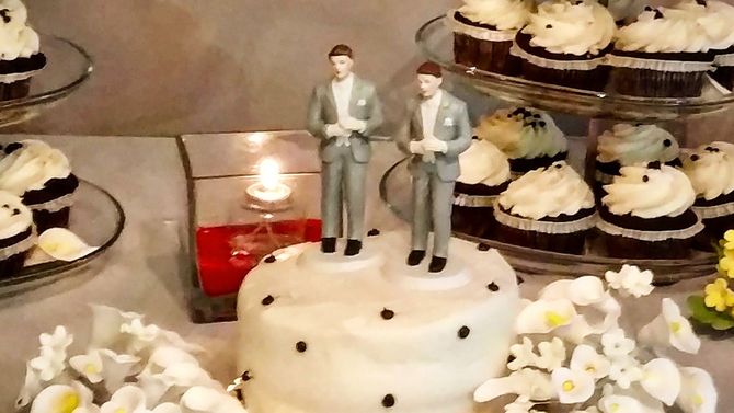 グレーのスーツに身を包んだ2人の新郎が、同性のゲイカップルのために小さな白いウェディングケーキを飾る