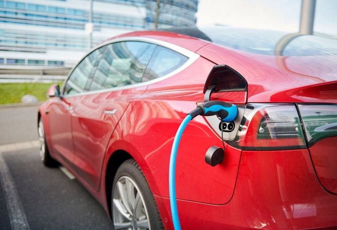 2019年12月10日、デュッセルドルフのビジネス街に駐車された赤いテスラモデルSは、青い電源コードで充電ステーションに接続されている