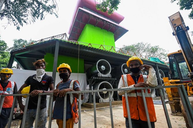 2021年8月23日、ニューデリーで、汚染シーズンに空気を浄化するために建設された高さ25メートルの「アンチスモッグ・タワー」の前に立つ作業員たち。