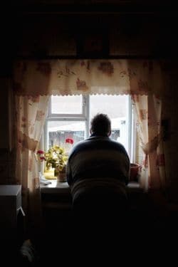 窓辺で外を眺める高齢男性