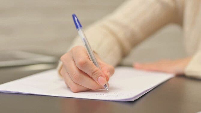 紙にペンで文字を書く女性の手