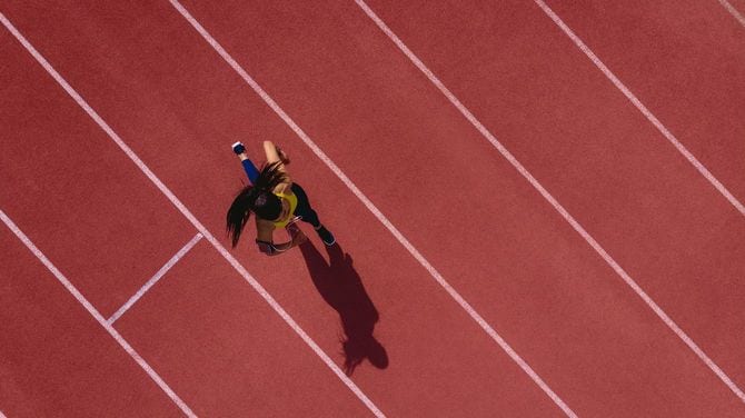 若い女性選手が音楽を聴きながら競技場のトラックを走る