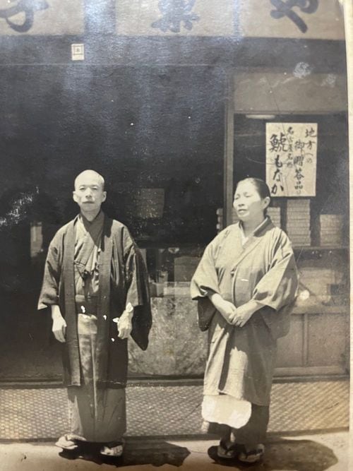 店舗の前に並ぶ創業者夫妻。店舗に貼ってあるポスターには「地方への御贈答品 名古屋名物 鯱もなか」と書いてある