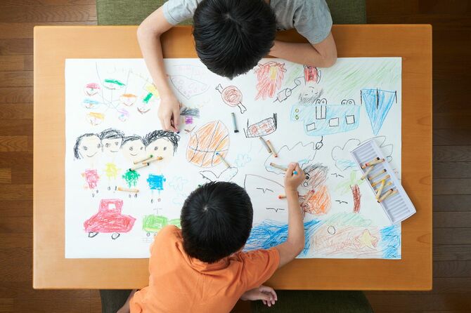 巨大な画用紙に同時に絵を描き込んでいる二人の子供