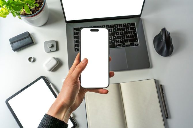 ラップトップを置いた机に座り、スマホを立ち上げている人の手元