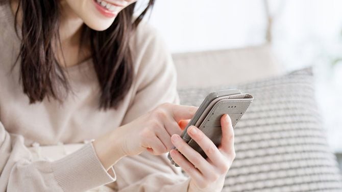 ソファーに座り、笑いながらスマホを使用している若い女性