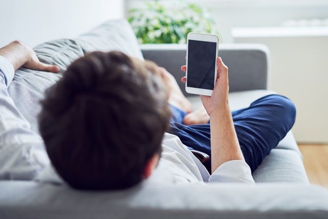 ソファに横たわってスマートフォンを使用する人