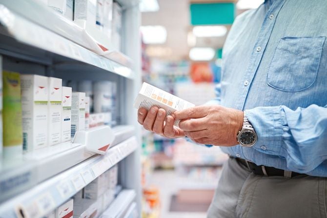薬局の棚の前で、薬の箱に描かれた文字を読んでいる男性