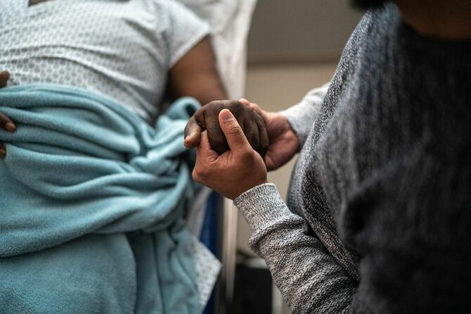 病院のベッドに横たわる息子の手を握る父親