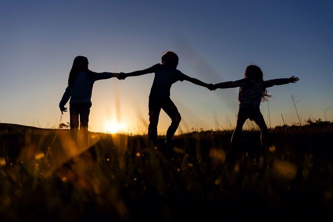 夕暮れ時の原っぱで手をつないで遊ぶきょうだいのシルエット