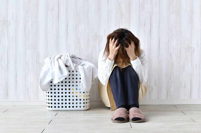 洗濯物かごの横でうずくまり、頭をかき乱している女性