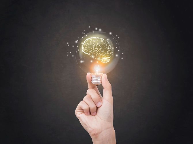 脳が描かれた光る電球を持つ手