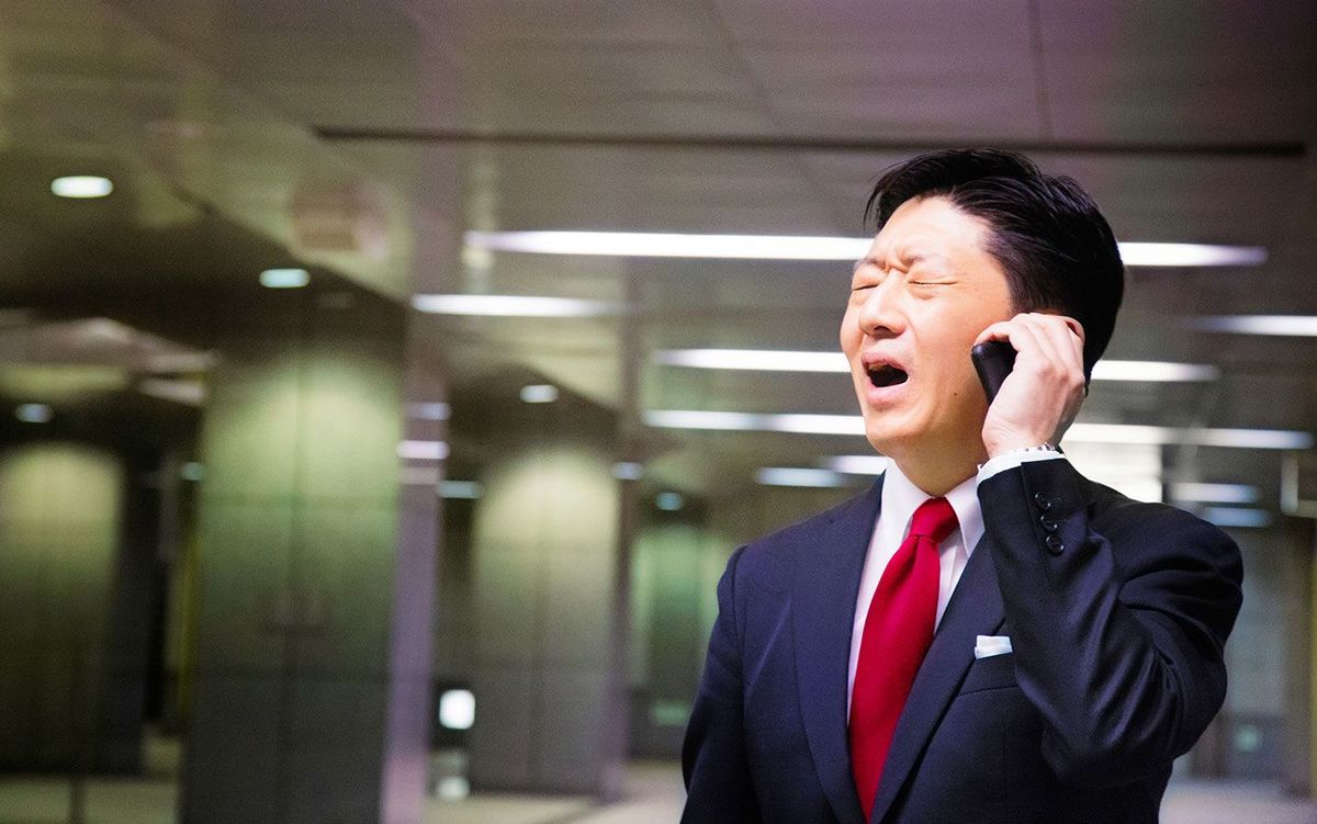 つらそうな表情で携帯電話で対応するビジネスマン