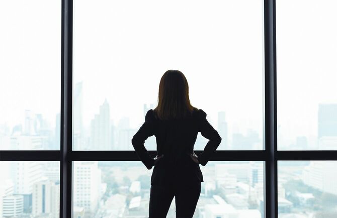 高層ビルの窓から下界を見下ろしている女性の後ろ姿