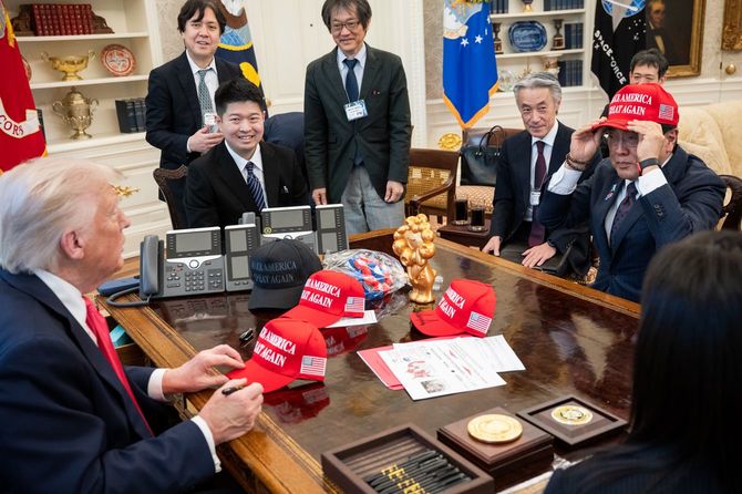 ドナルド・トランプ大統領が大統領執務室で日本の赤沢了生経済財政政策担当大臣および代表団と会談後、MAGAの帽子を配る場面