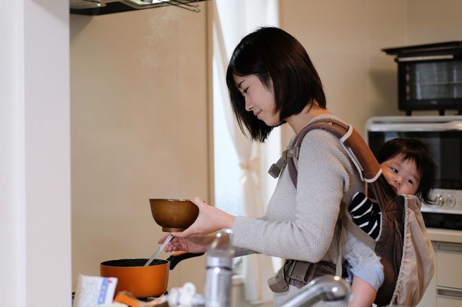 子どもを背負いながら調理をする母親