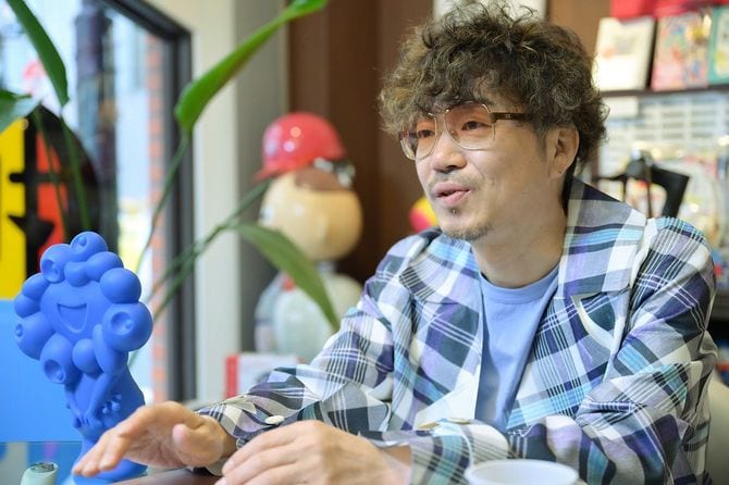 インタビューに応じる「ヘソプロダクション」代表の稲本ミノルさん。アイディア商品でヒットを重ねるヒットメーカーだ。トランプ大統領への手土産として話題を集めた「金色のミャクミャク貯金箱」は1000個が完売した。