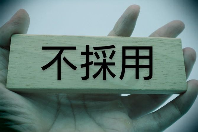 不採用と書かれた木製ブロックを手に持つ人