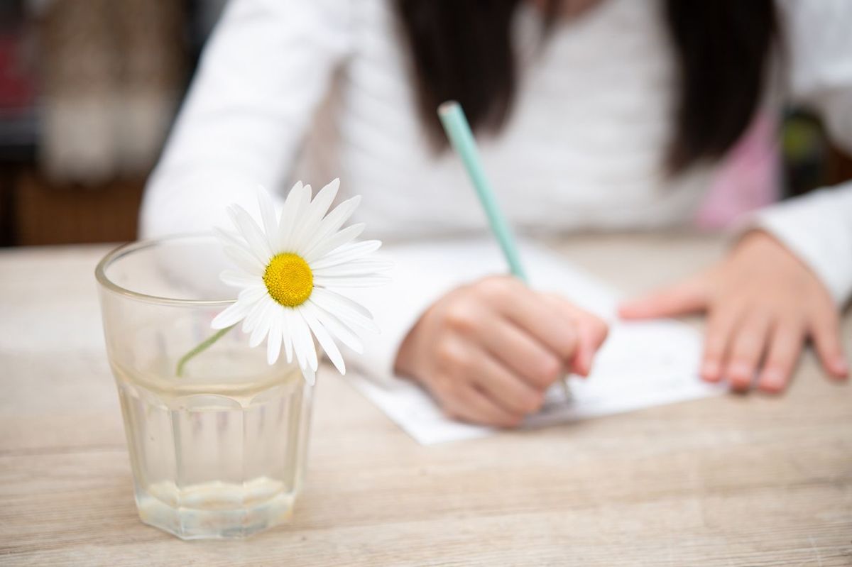 グラスに一輪挿しの花を置いた机で勉強する少女